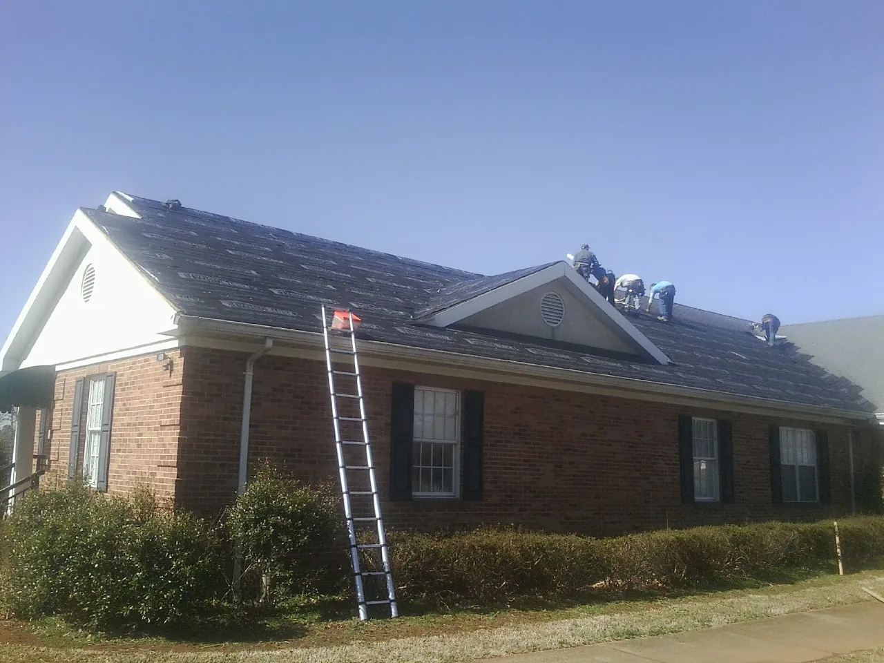 Crew tearing shingles off a brick ranch roof with a ladder set — Metal Roof Repair work by our crew in Hancock