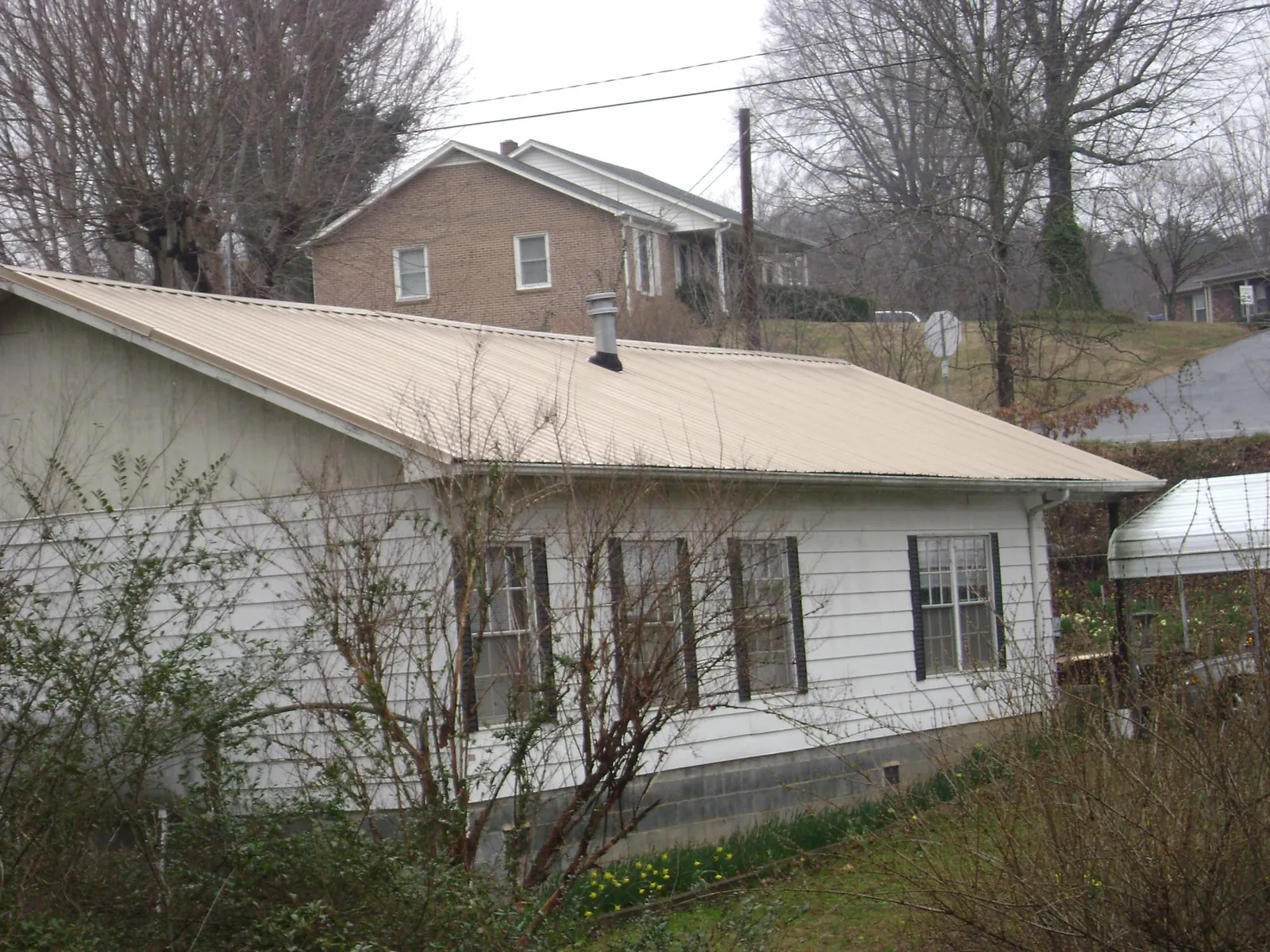 Tan metal roof on a white sided house set into a hillside — Commercial Roofing by Roofing Brothers in Hancock