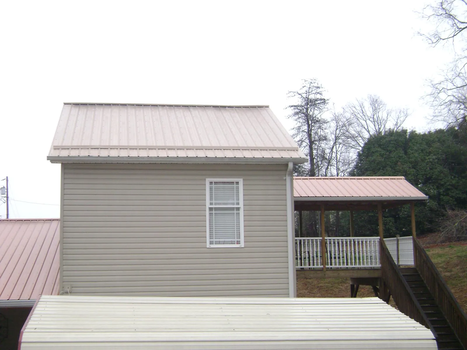 Tan metal roofs on a two story addition and attached porch, from a Roof Replacement job in Hancock
